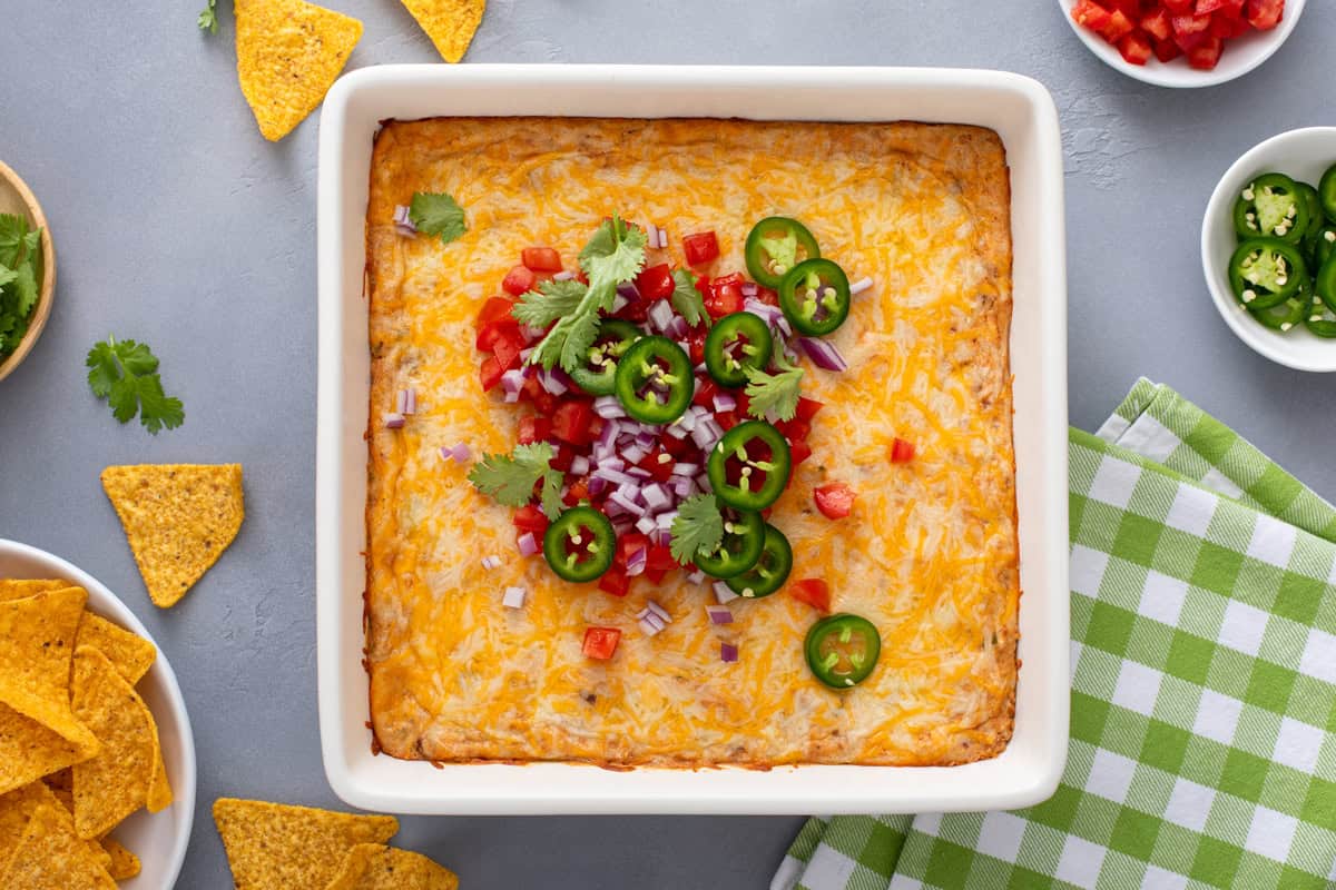 Overhead view of baked texas trash dip in a white baking dish, topped with diced tomato, red onion, and sliced jalapeños.