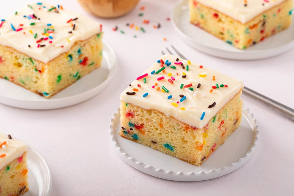 Plated slices of funfetti sheet cake topped with rainbow sprinkles.