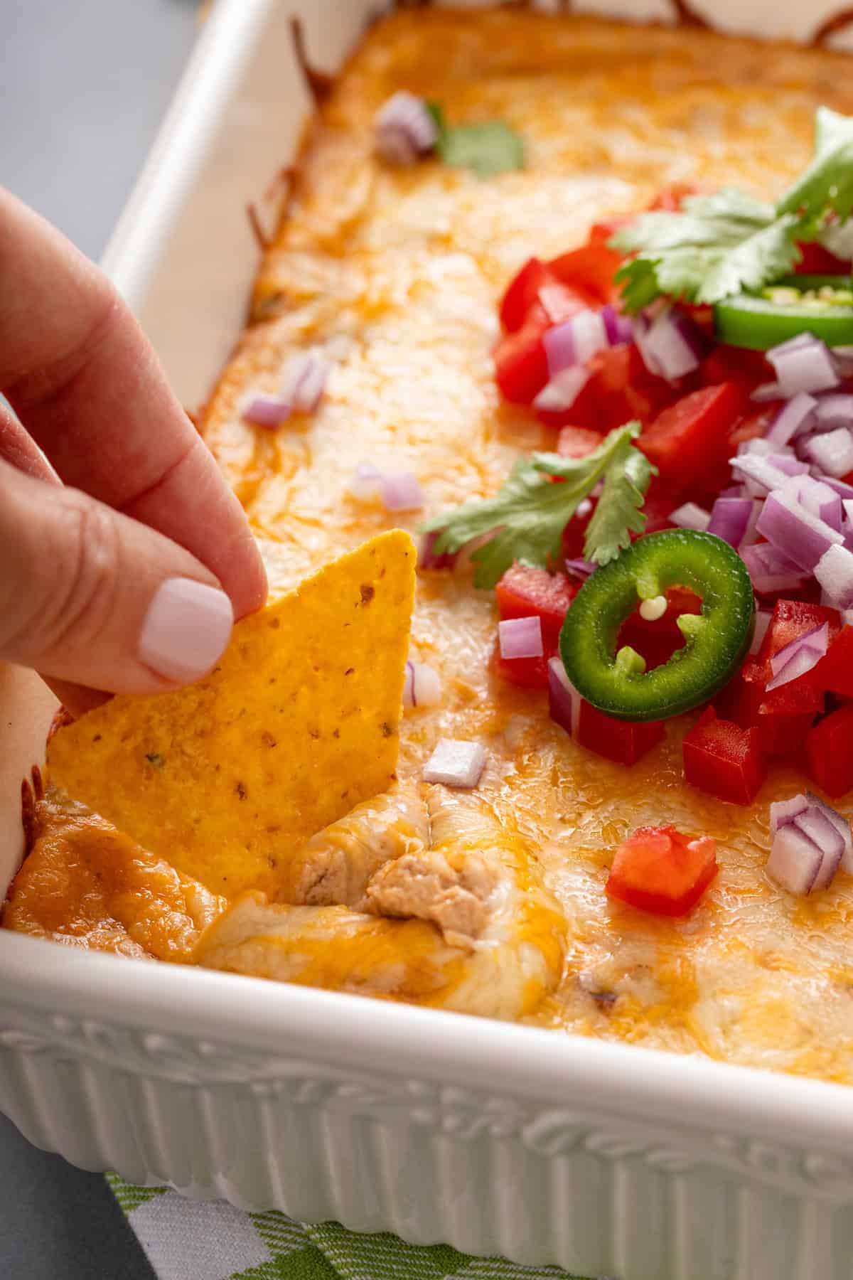Person using a tortilla chip to dip into texas trash dip in a white baking dish.