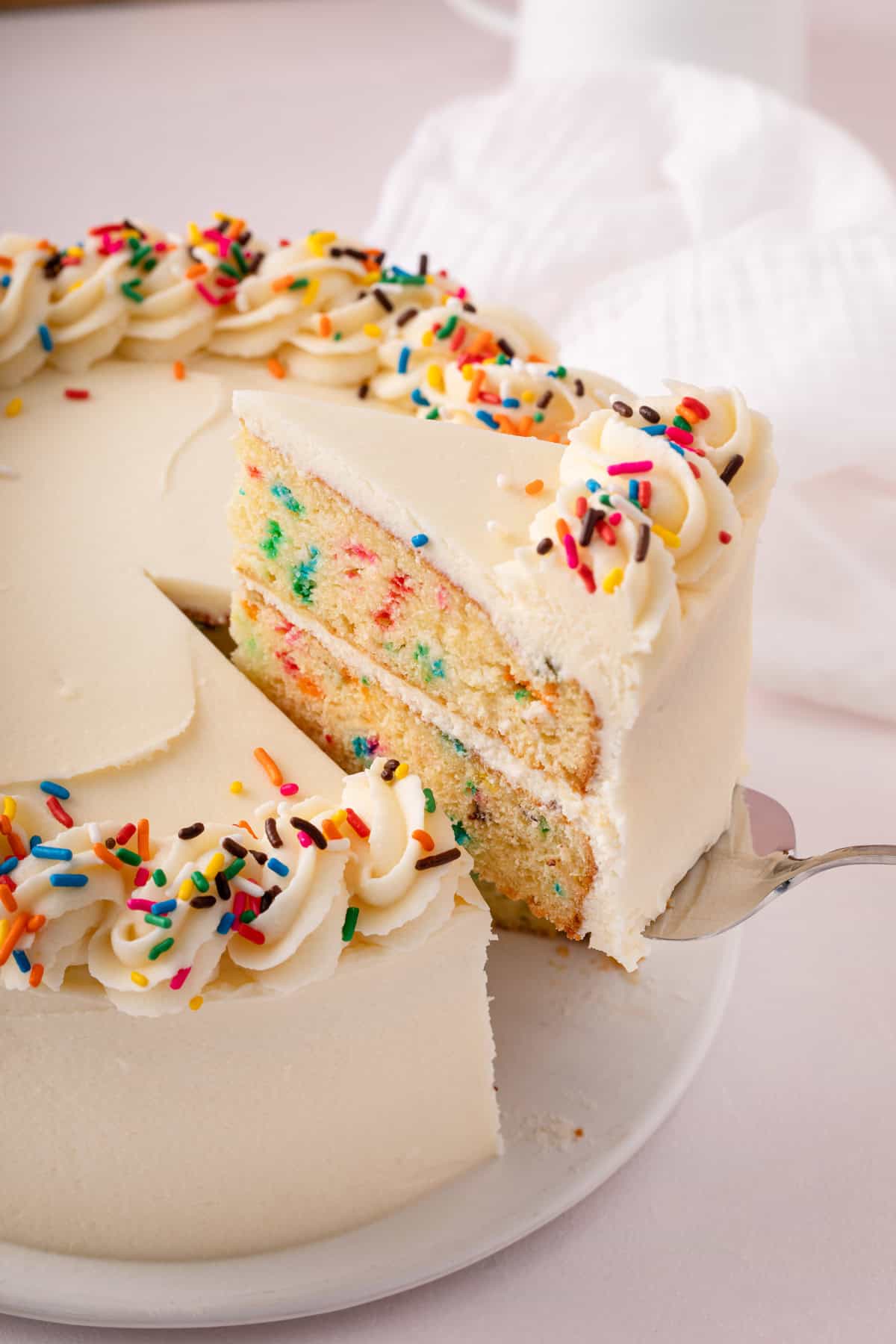 Cake server removing a slice of funfetti layer cake from the cake.
