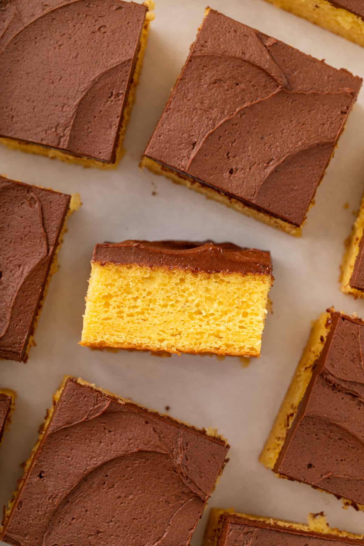 Sliced yellow sheet cake topped with chocolate frosting. One slice in the center is turned on its side.
