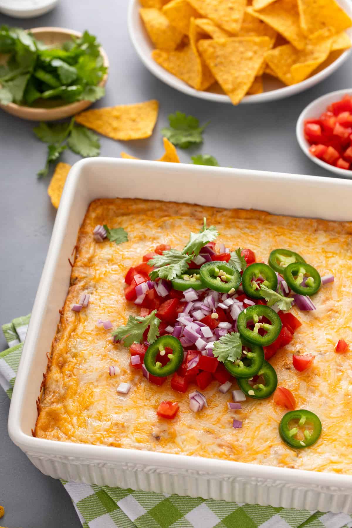 White baking dish filled with texas trash bean dip and topped with sliced jalapeños, red onions, and tomatoes.