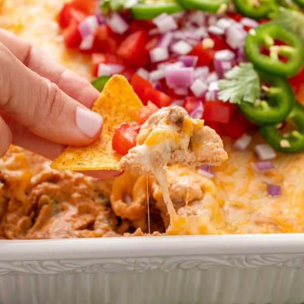 Hand lifting a bite of texas trash dip out of a white baking dish using a tortilla chip.