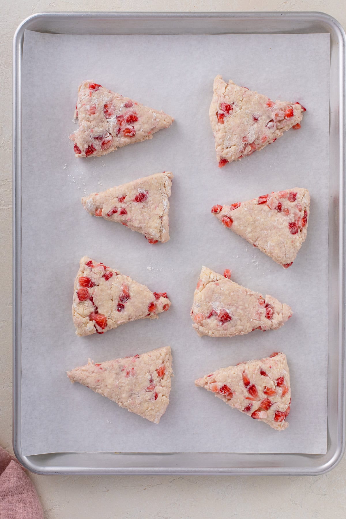 8 triangles of strawberry scone dough arranged on a parchment-lined baking sheet, ready to go in the oven.