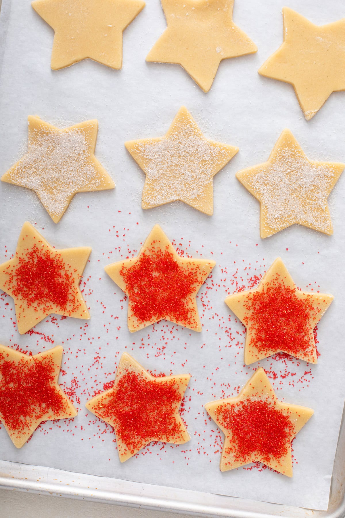 Unbaked star sugar cookie cutouts on a parchment lined baking sheet, topped with red and white sparkling sugar.