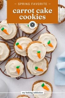 Overhead view of frosted carrot cake cookies decorated with a frosting carrot arranged on a wire rack. Text overlay includes recipe name.