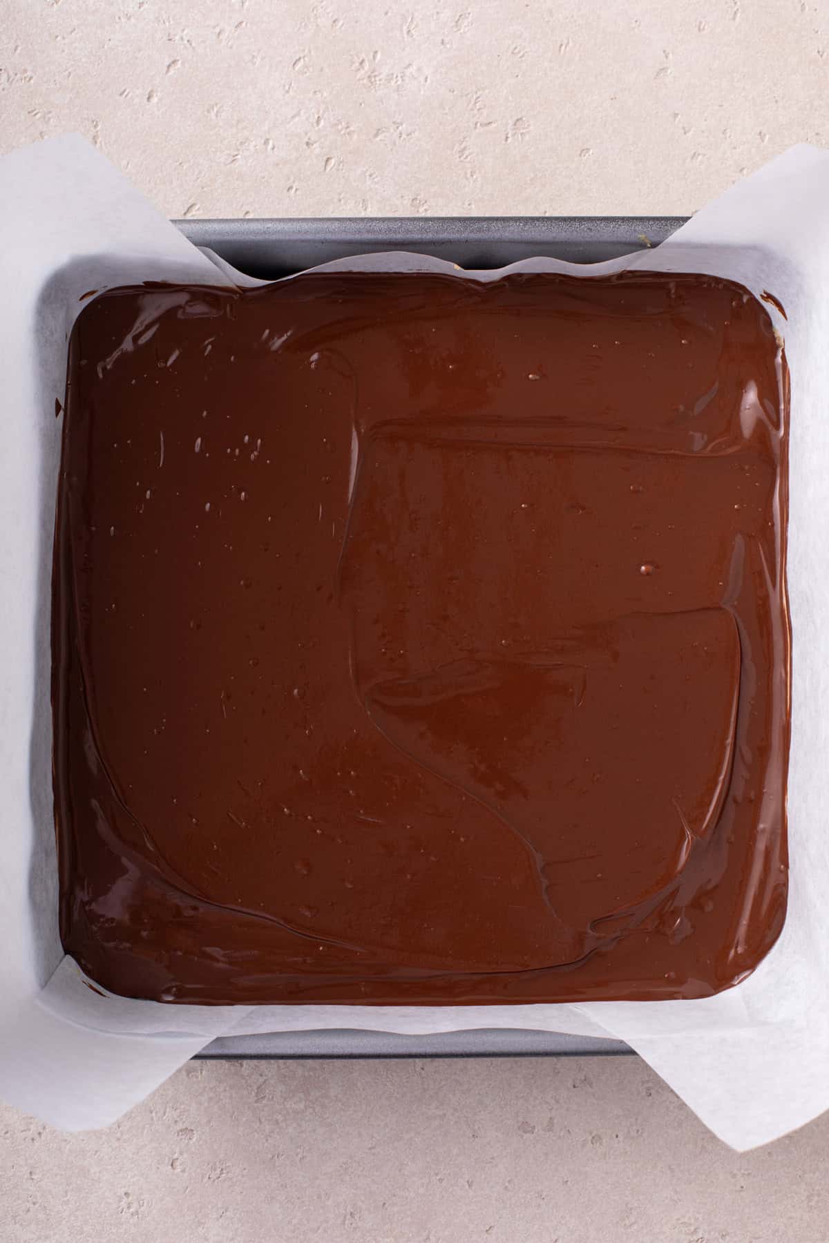 Chocolate spread over lunch lady bars in a parchment-lined square pan.