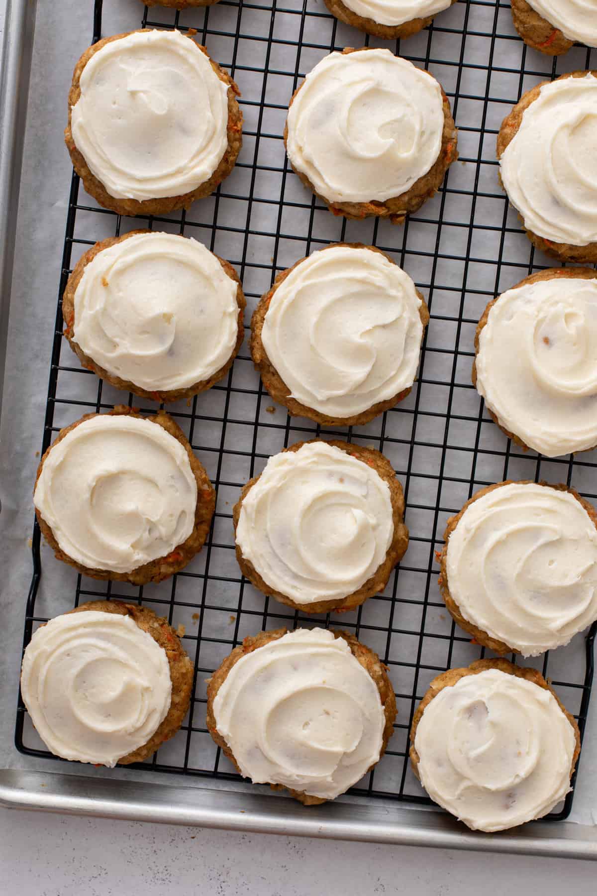 Cream cheese frosting spread onto the top of carrot cake cookies arranged on a wire rack.