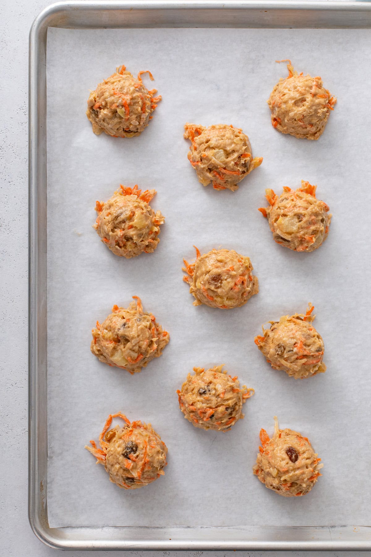 Carrot cake cookie dough portioned in scoops on a parchment-lined baking sheet.
