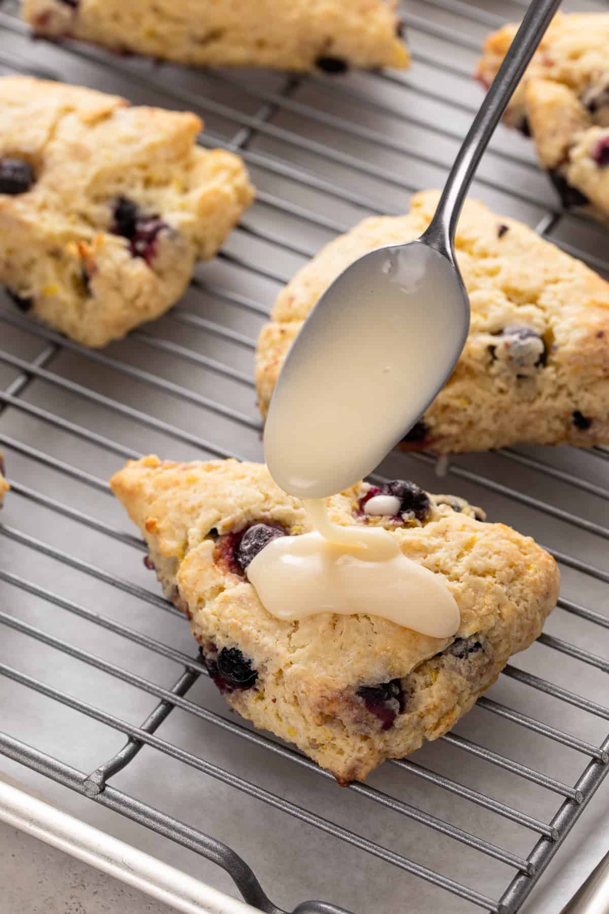 Lemon glaze being spooned over the top of lemon blueberry scones.