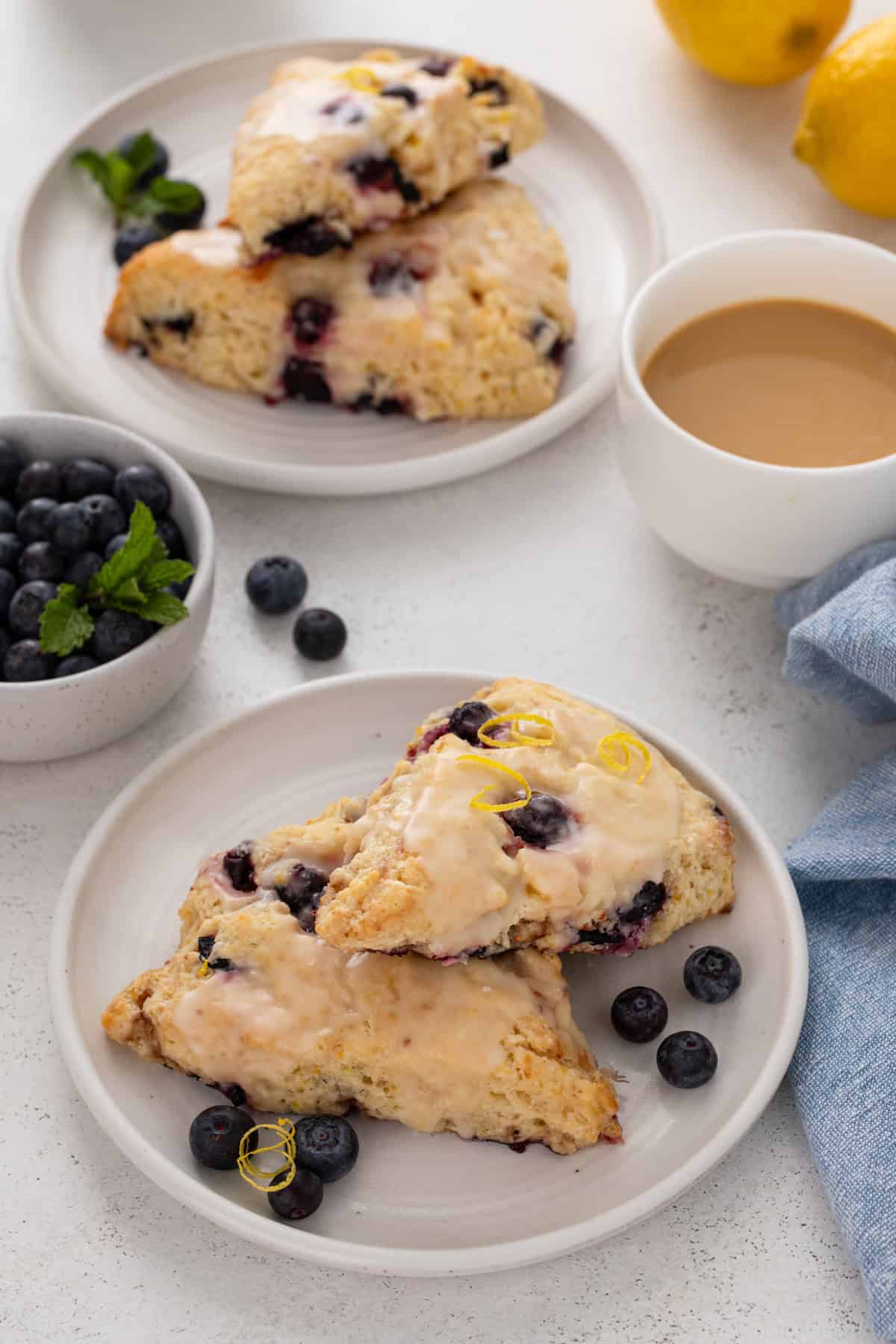 White plates, each holding two lemon blueberry scones, with a cup of coffee in the background.