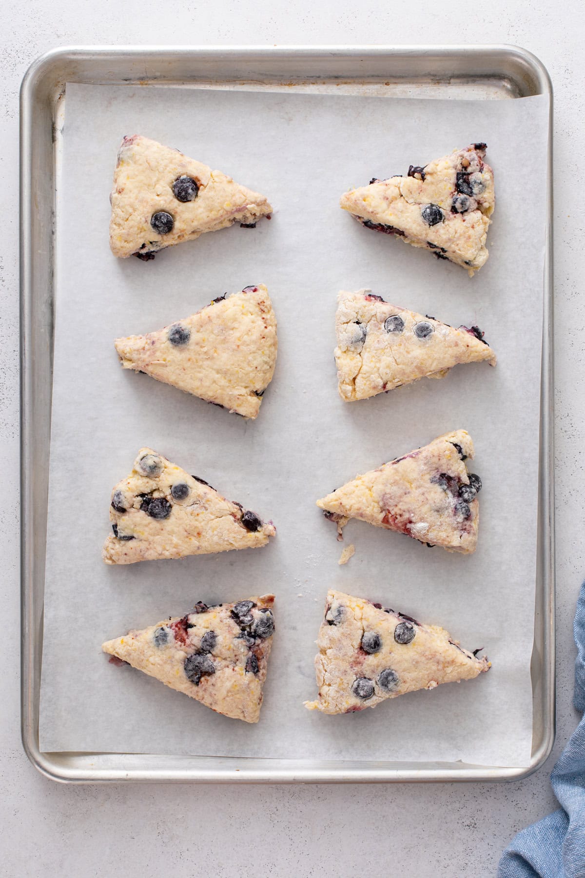 Unbaked lemon blueberry scones on a parchment-lined baking sheet, ready to go in the oven.