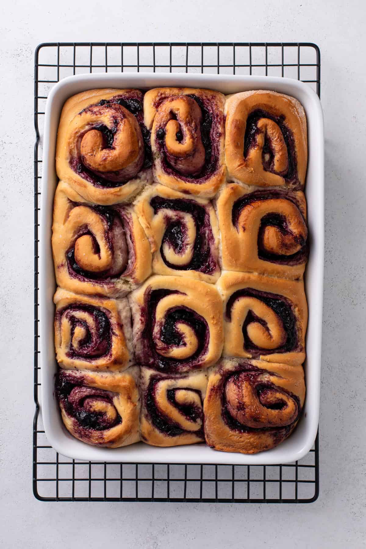 Baked blueberry sweet rolls in a white pan cooling on a wire rack.