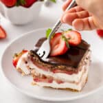 Person cutting in the corner of a slice of strawberry eclair cake with a fork.