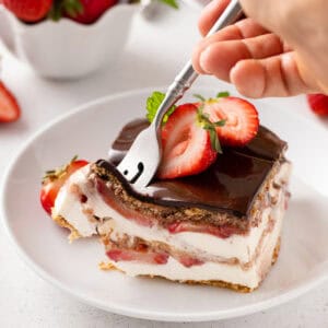 Person cutting in the corner of a slice of strawberry eclair cake with a fork.