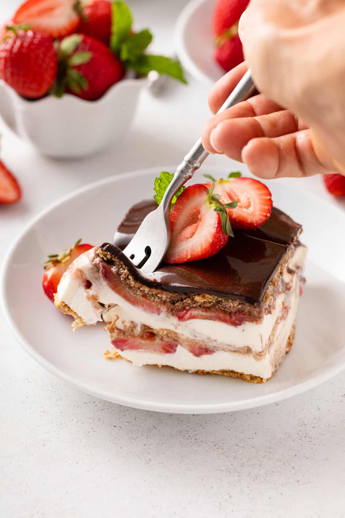 Fork cutting into the corner of a slice of eclair cake garnished with fresh strawberries.