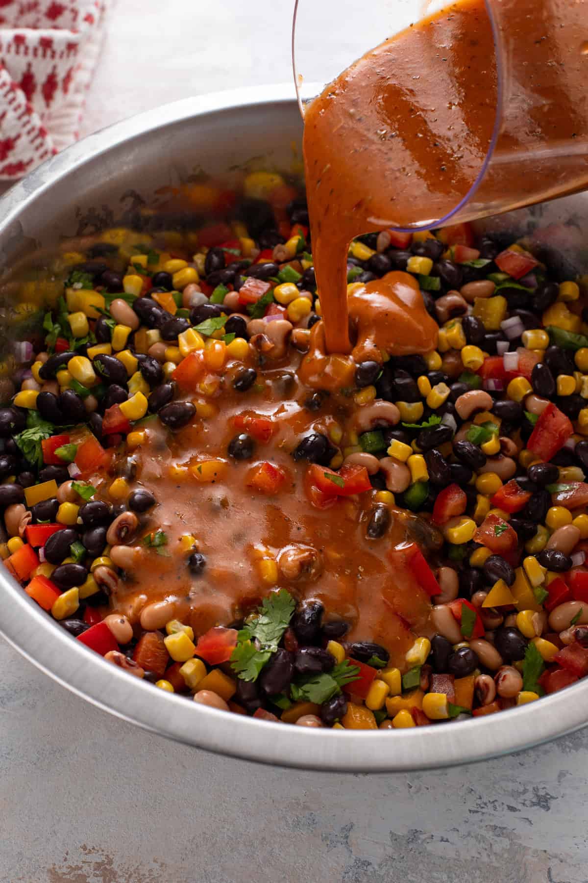 Dressing being poured over cowboy caviar ingredients in a mixing bowl.