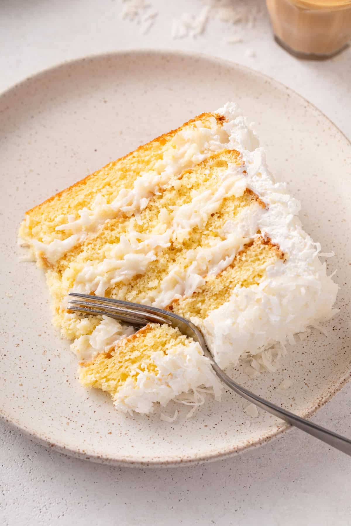 Fork cutting into a plated slice of sour cream coconut cake.