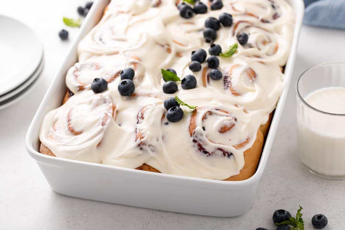 Blueberry sweet rolls topped with cream cheese frosting and garnished with fresh blueberries.