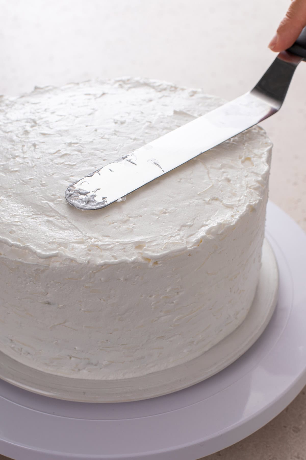 Coconut frosting being spread over a layered coconut cake.