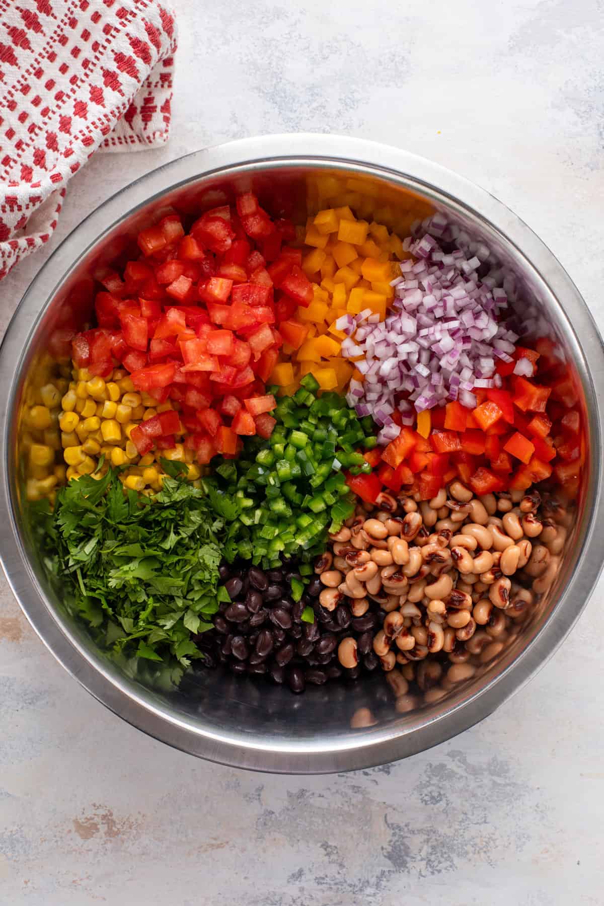 Ingredients for cowboy caviar added to a large metal mixing bowl.
