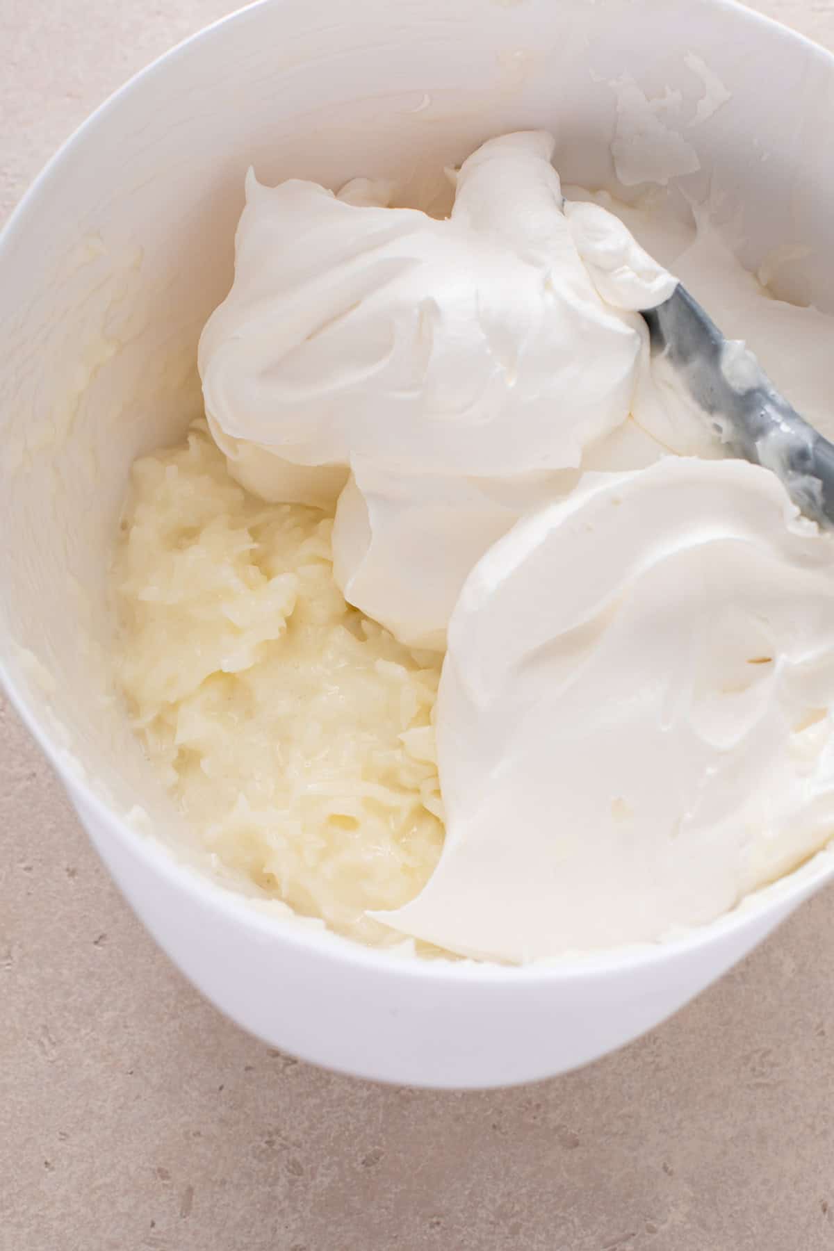 Whipped topping being added to a bowl of sour cream and coconut filling.