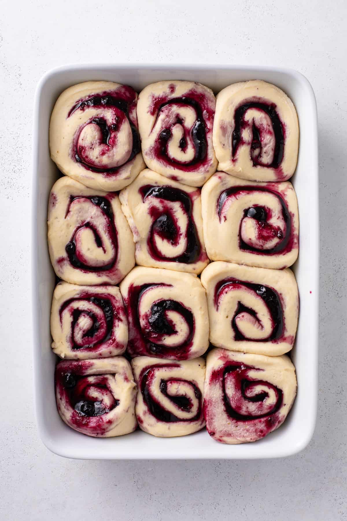 Risen blueberry sweet rolls in a white baking pan, ready to go in the oven.