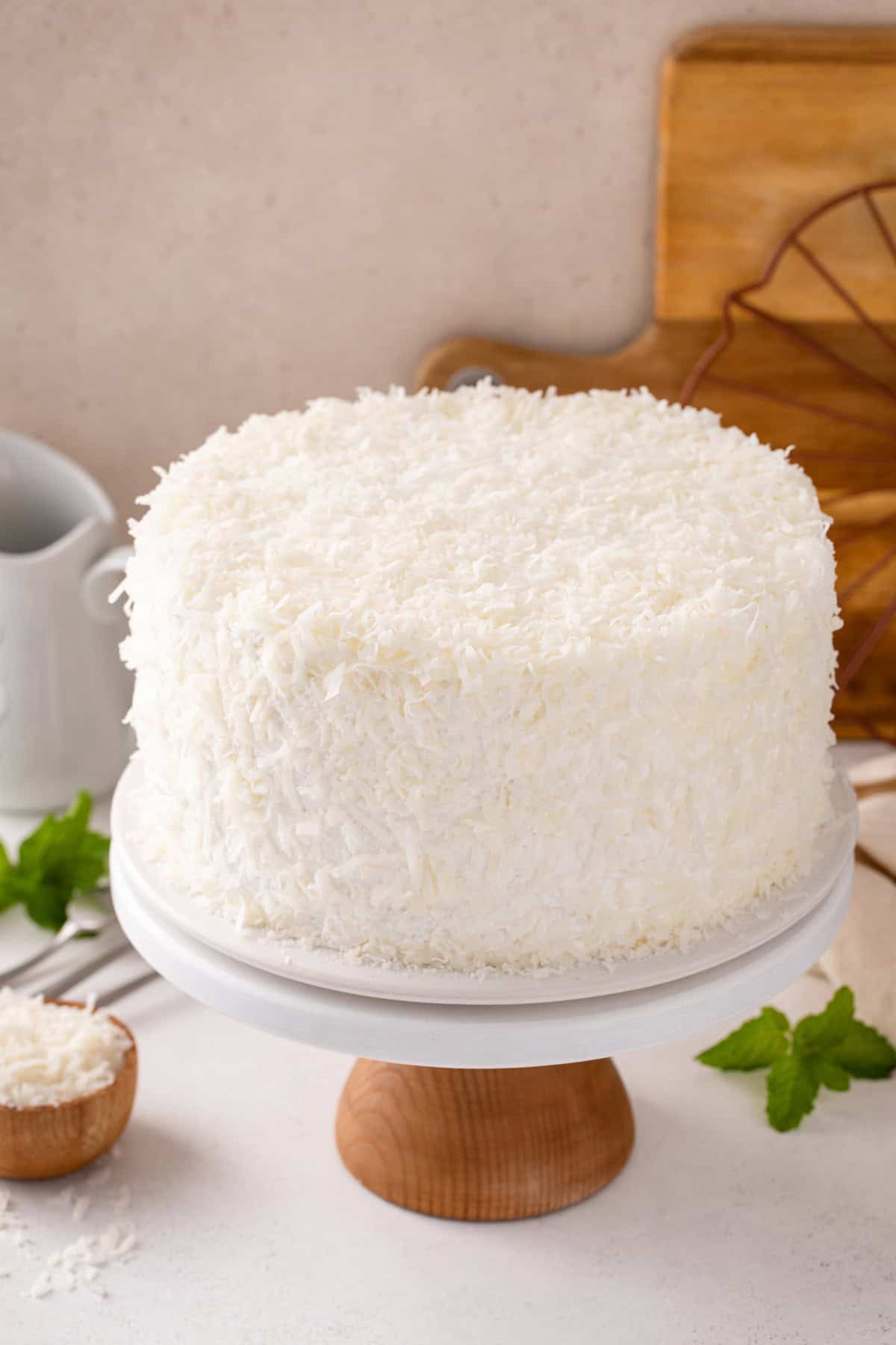 Sour cream coconut cake covered with shredded coconut set on a cake stand.