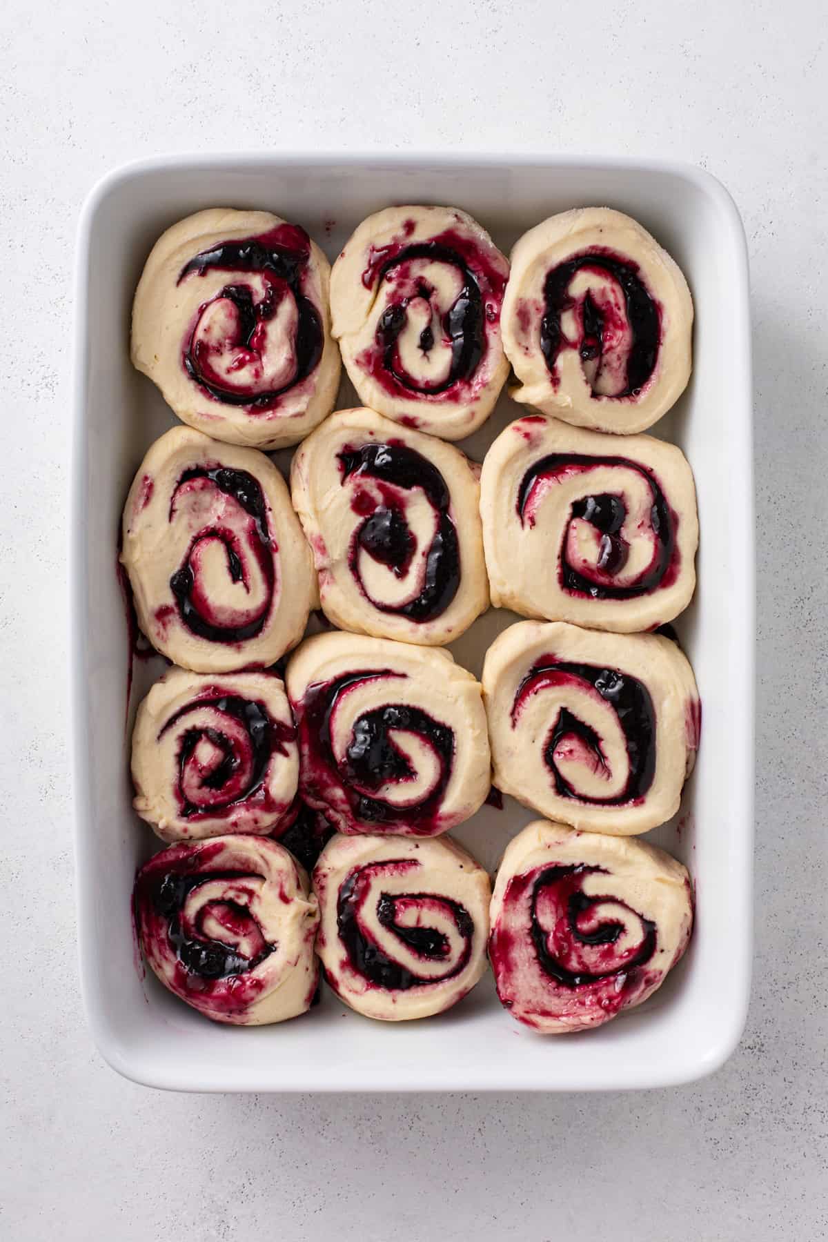 Assembled blueberry sweet rolls in a white baking dish, ready to rise.