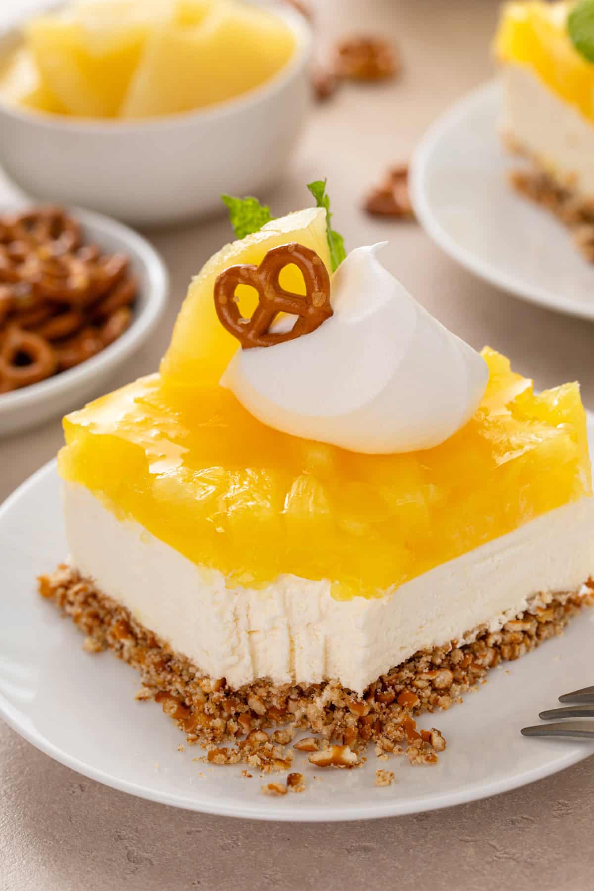 Close up of a plated slice of pineapple pretzel salad garnished with whipped cream, with a bite taken from the corner.