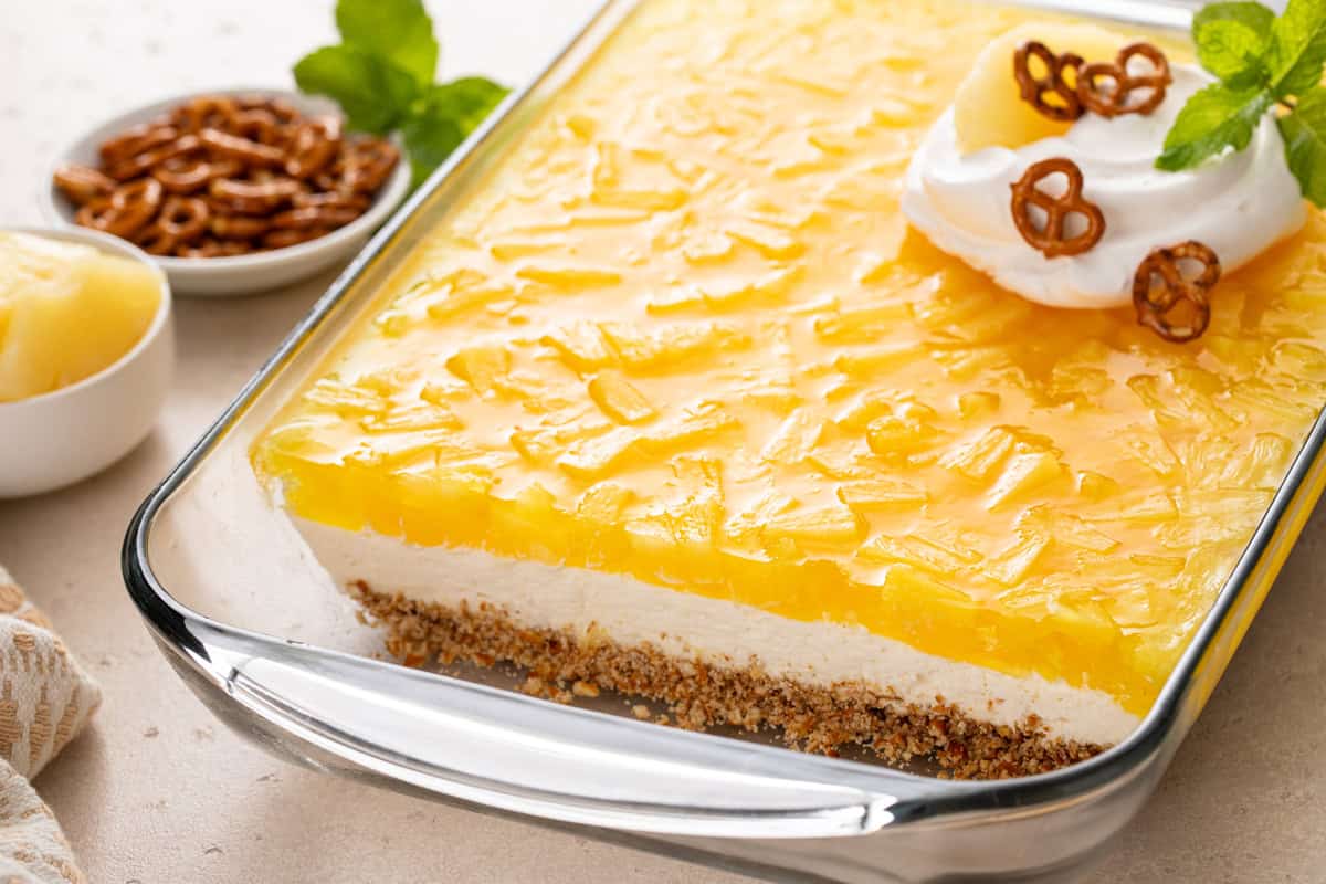 Pineapple pretzel salad in a glass pan, with several pieces removed so you can see the layers of the dessert.