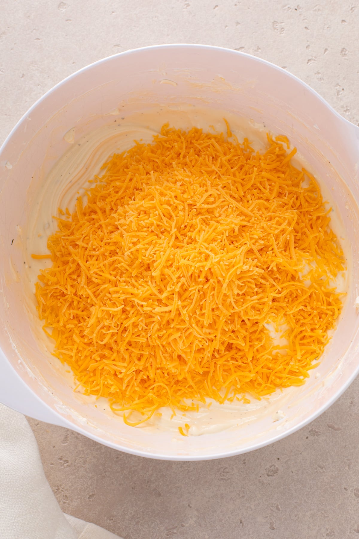 Shredded cheese added to a bowl of beer dip, ready to be mixed in.