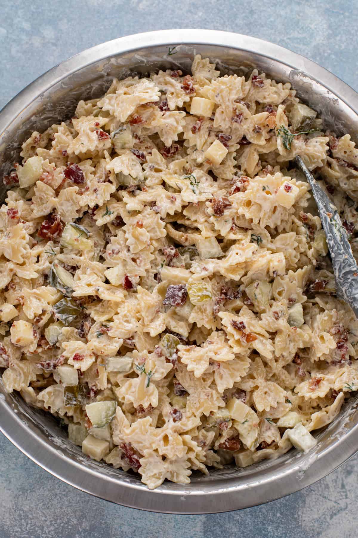 Dill pickle pasta salad being stirred together in a large mixing bowl.
