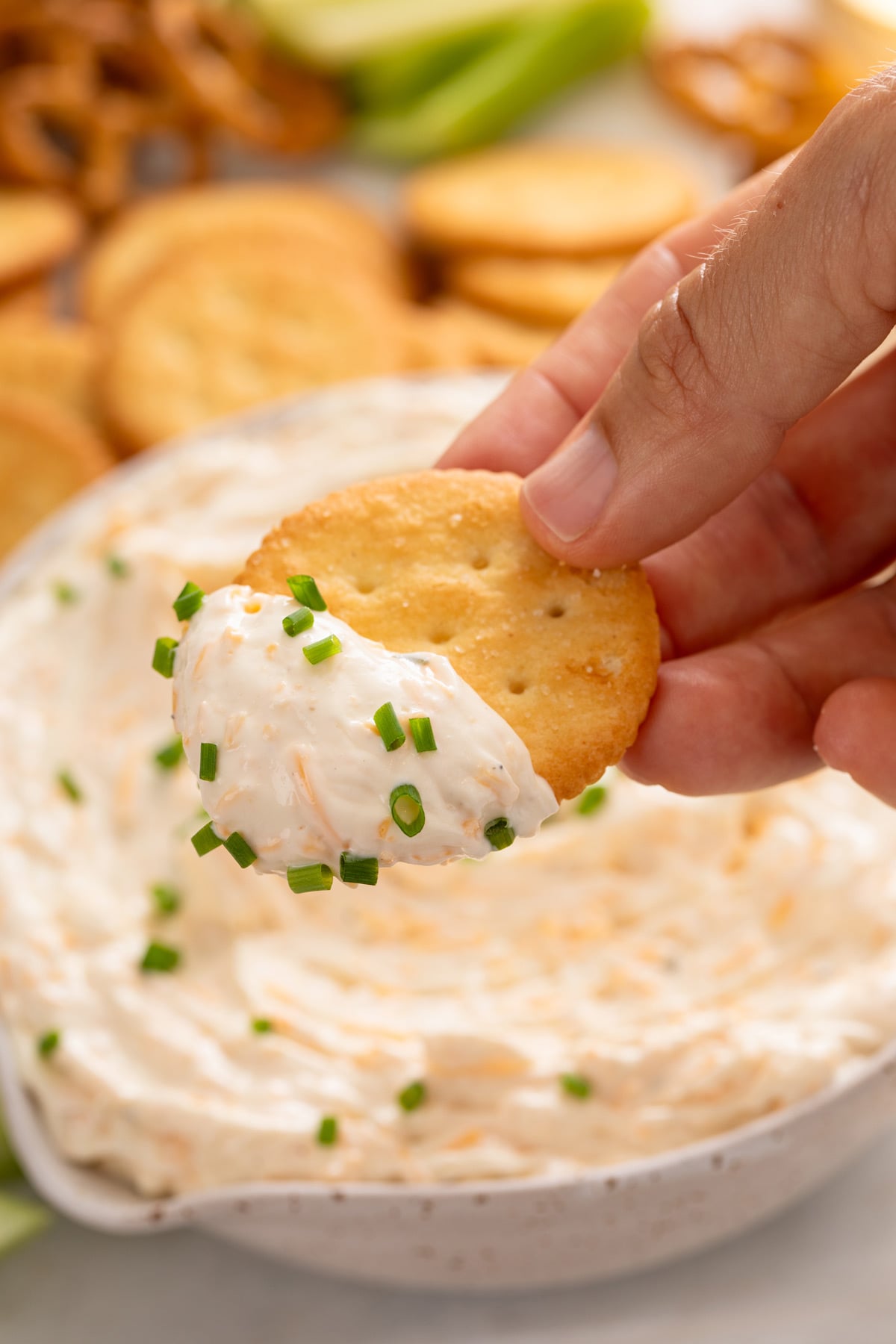 Hand holding a cracker with ranch beer cheese dip on it.