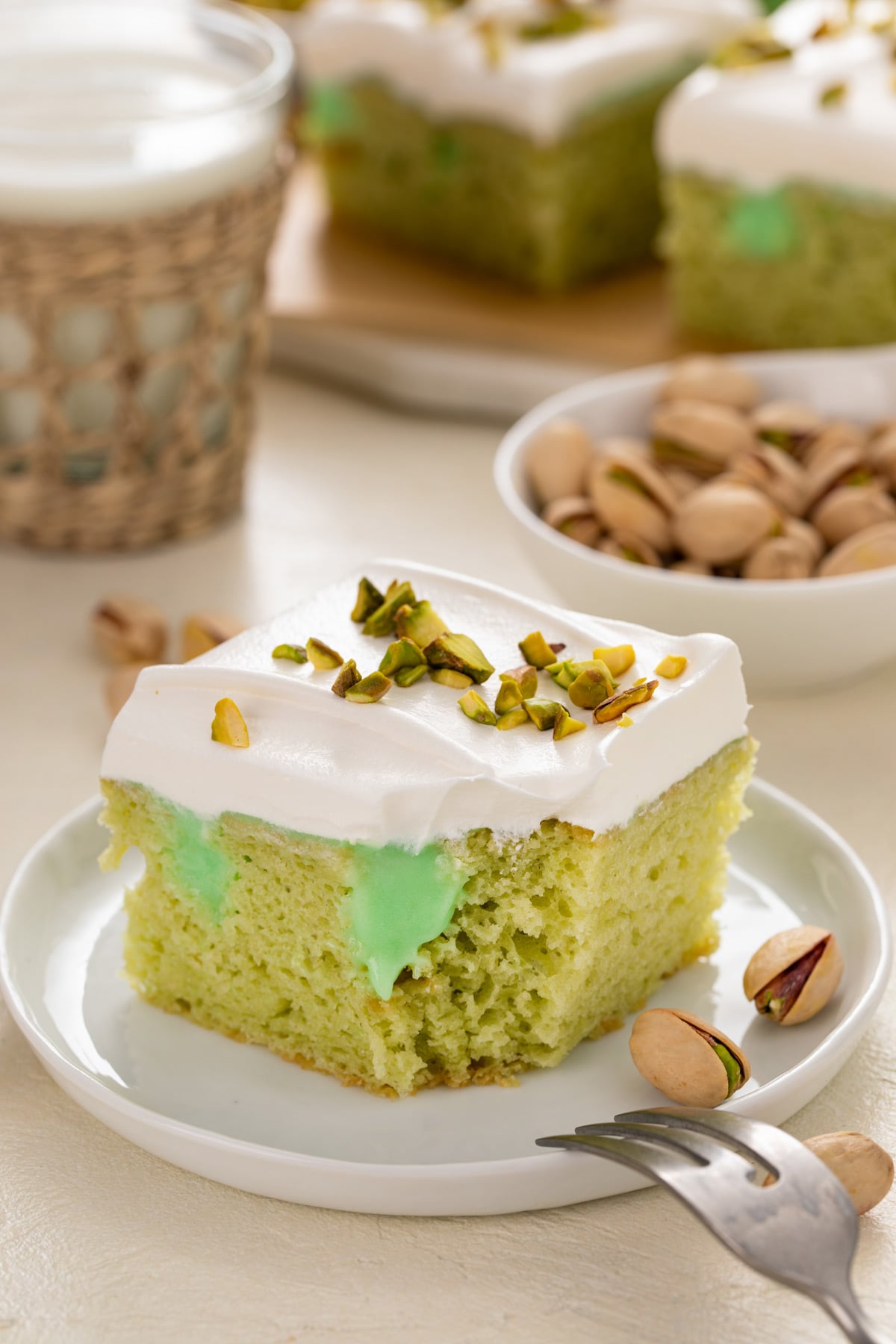 Bite taken from the corner of a slice of pistachio poke cake on a white plate.