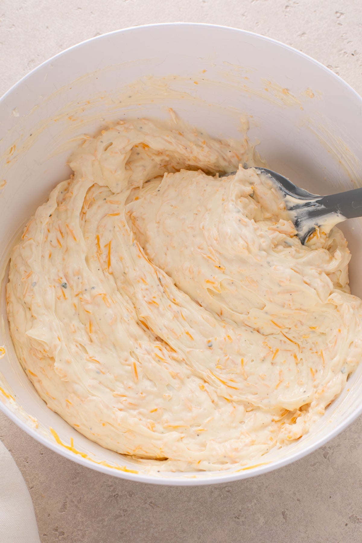 Spatula stirring together ranch beer cheese dip in a white mixing bowl.