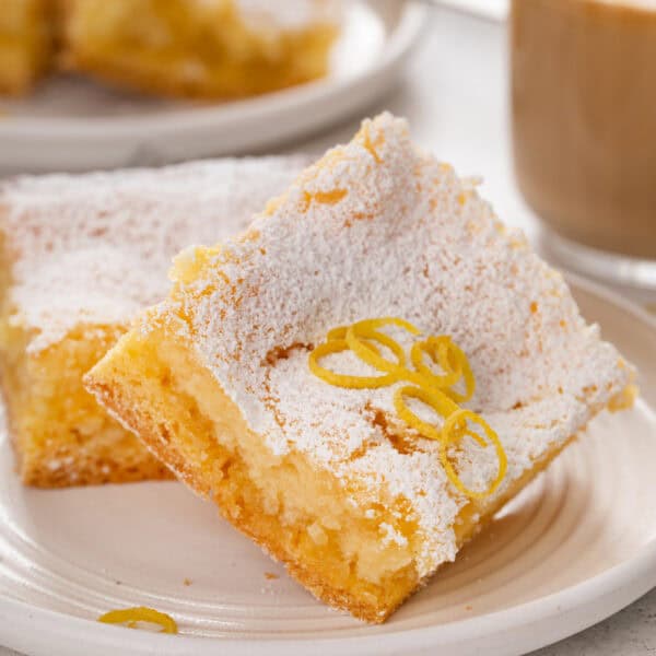 Close up of 2 slices of lemon gooey butter cake on a white plate.