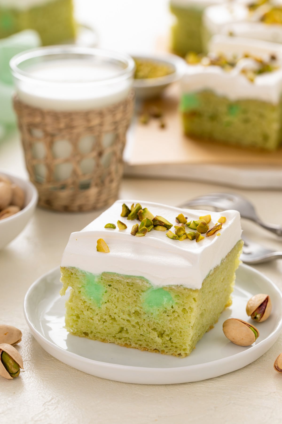 Plated slice of pistachio poke cake with a glass of milk in the background.