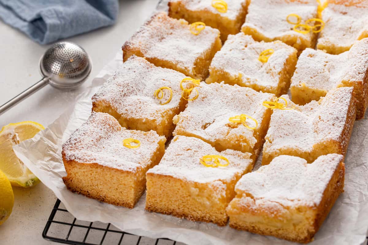 Slices of lemon gooey butter cake on a wire rack with the tops dusted with powdered sugar.
