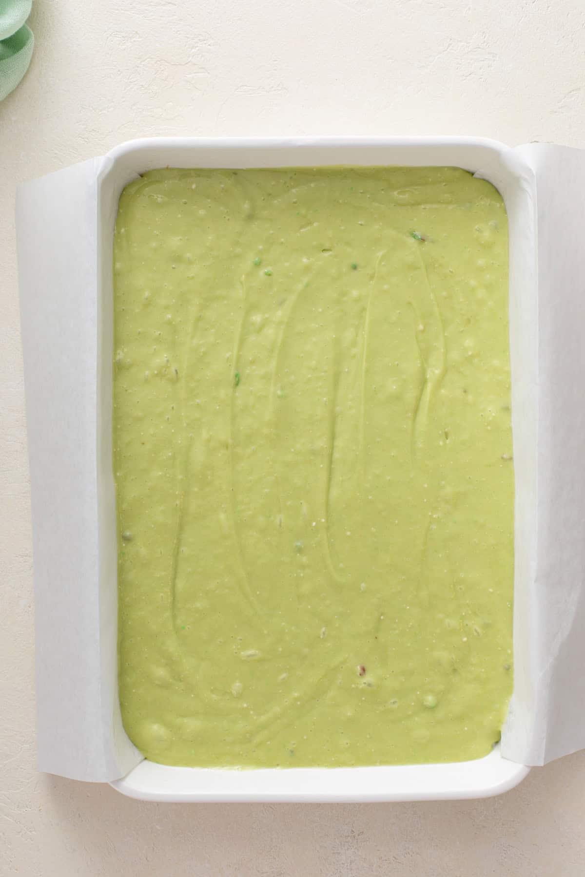 Pistachio poke cake batter in a 9x13-inch cake pan, ready to be baked.