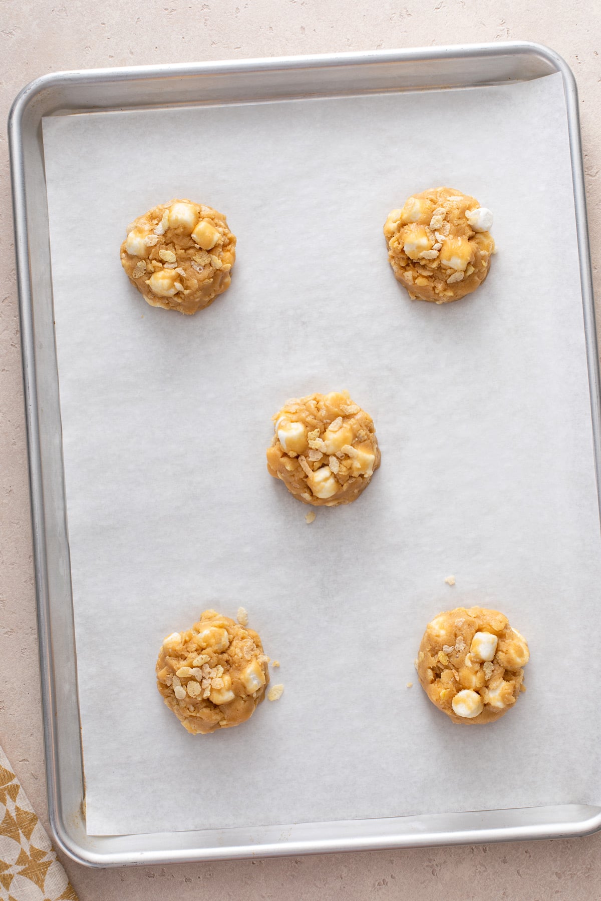 5 scoops of rice krispie cookie dough on a parchment-lined baking sheet.