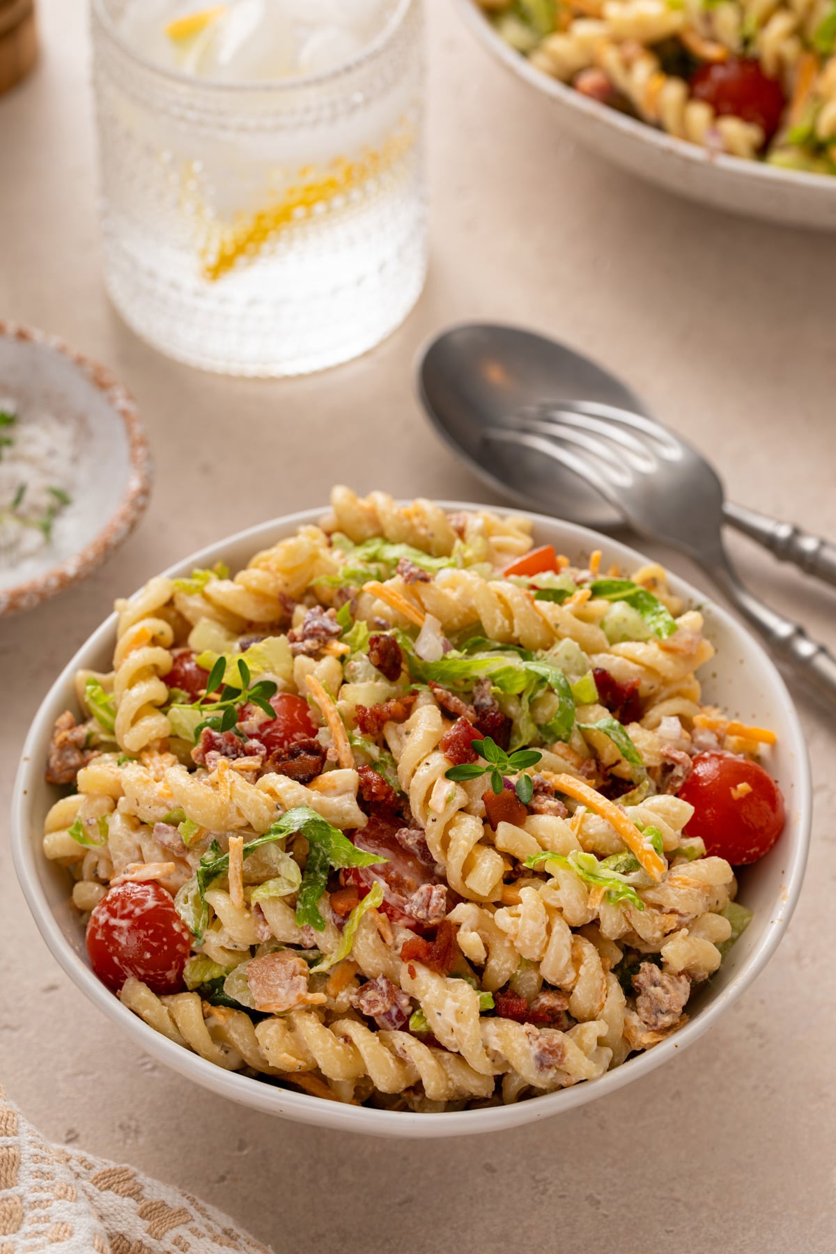 Small bowl of BLT pasta salad on a countertop next to a spoon and fork.