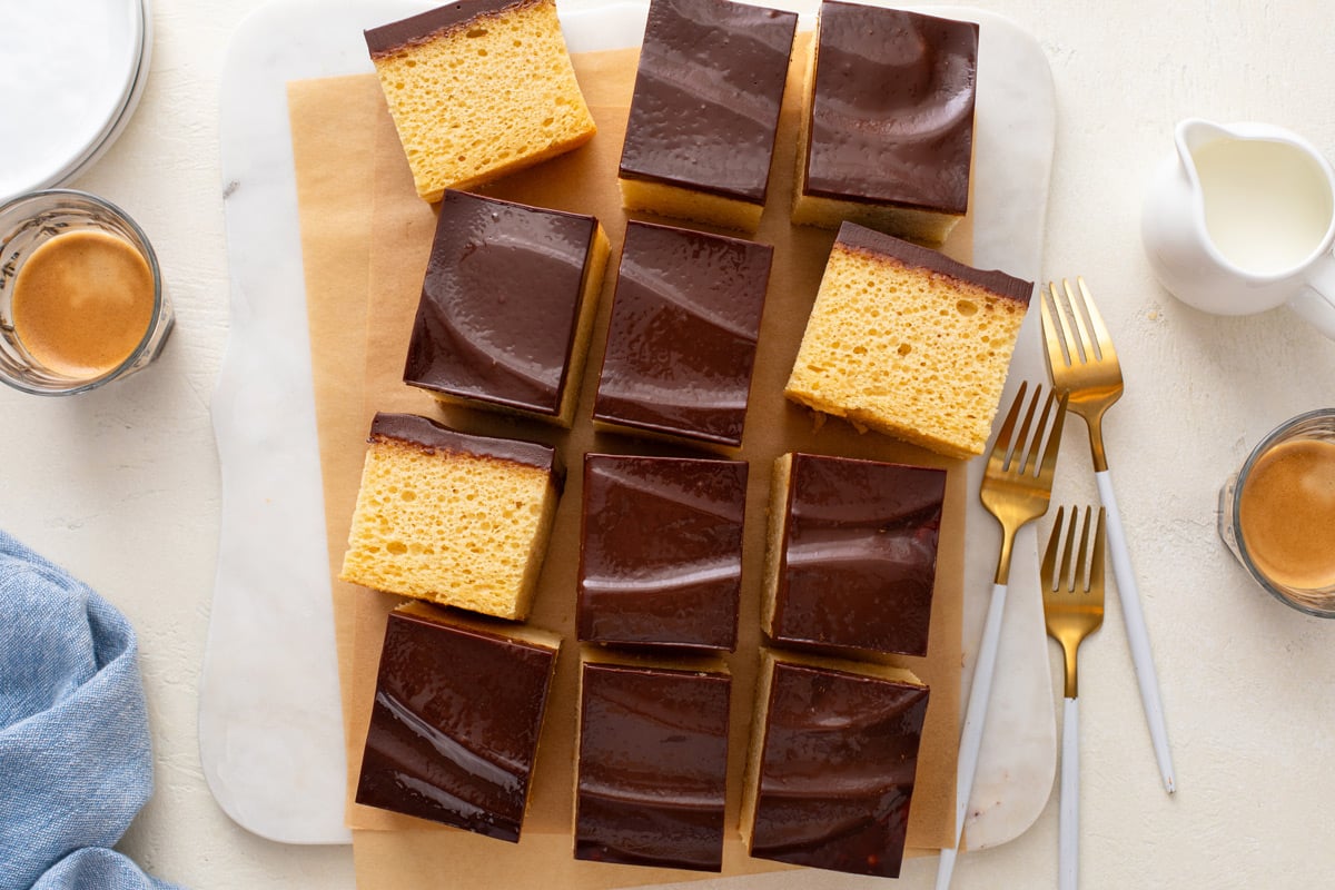 Overhead view of a sliced yellow sheet cake with chocolate frosting on a piece of parchment paper.