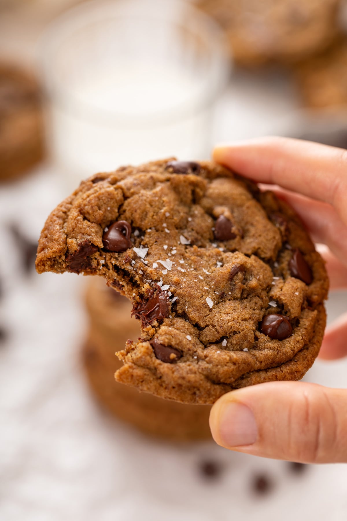 Hand holding up an espresso chocolate chip cookie with a bite taken from it.