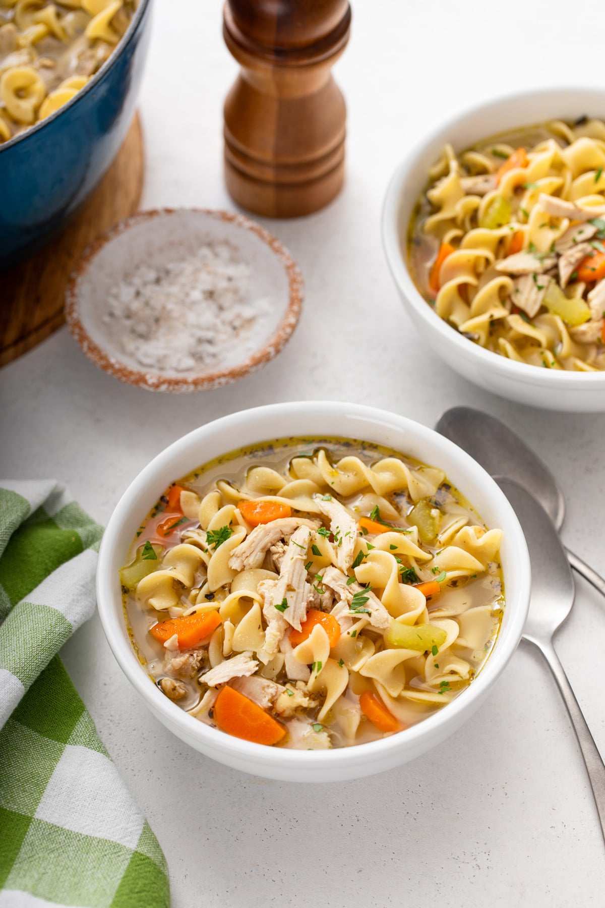 Two bowls of easy chicken noodle soup set on a countertop. A blue pot of the soup is just visible off to the side.