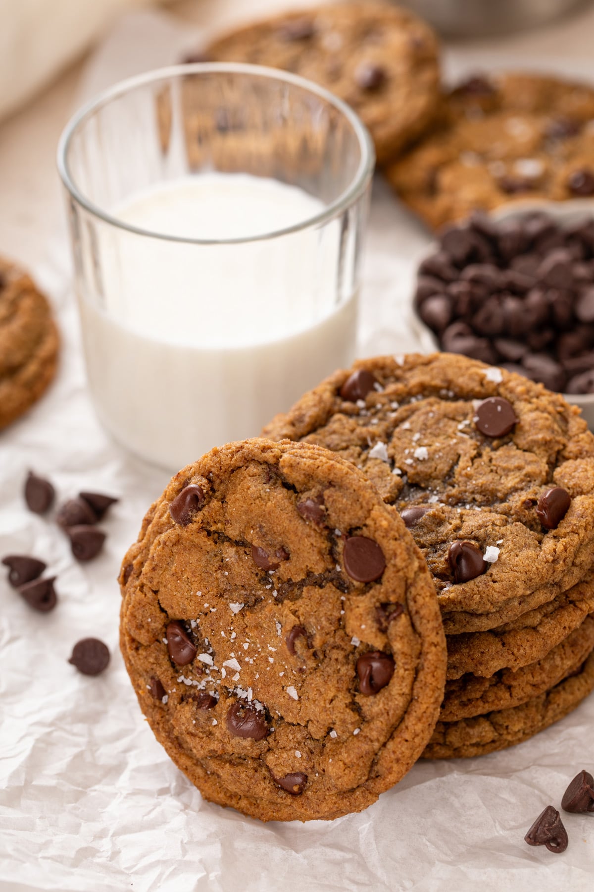 Four espresso chocolate chip cookies stacked by a glass of milk with a fifth cookie leaning against the stack.