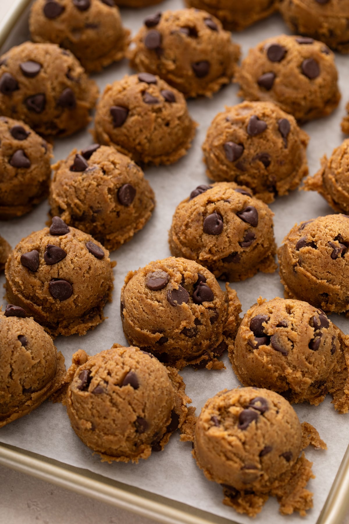 Balls of scooped espresso chocolate chip cookie dough lined up on a sheet pan.