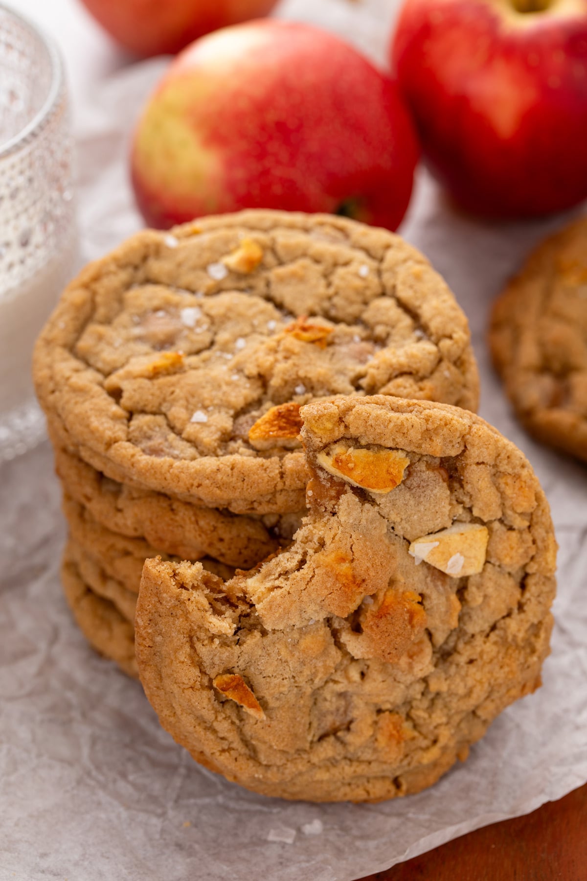 4 caramel apple cookies stacked next to a glass of milk. A 5th cookie with a bite taken out of it leans against the stack.