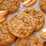 Caramel apple cookies on a sheet of parchment paper with sliced fresh apples.