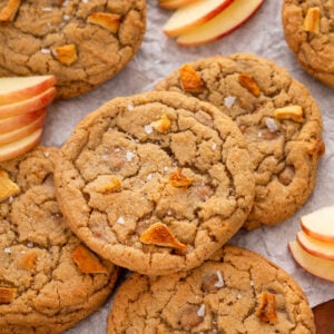 Caramel apple cookies on a sheet of parchment paper with sliced fresh apples.